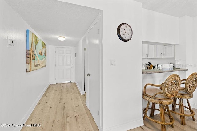 hall with light wood-type flooring and a textured ceiling