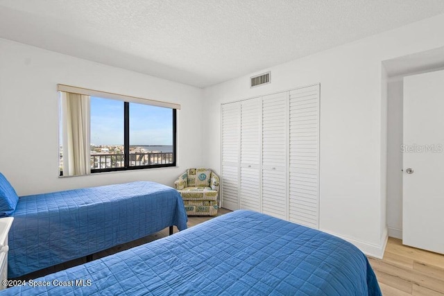 bedroom with a closet, a textured ceiling, and light hardwood / wood-style flooring