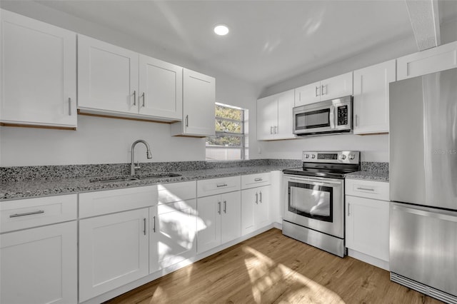 kitchen with light stone countertops, sink, appliances with stainless steel finishes, white cabinets, and light wood-type flooring