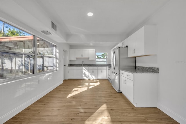 kitchen featuring white cabinets, stainless steel fridge, light wood-type flooring, and a wealth of natural light