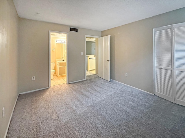 unfurnished bedroom featuring connected bathroom, sink, a textured ceiling, light carpet, and a closet