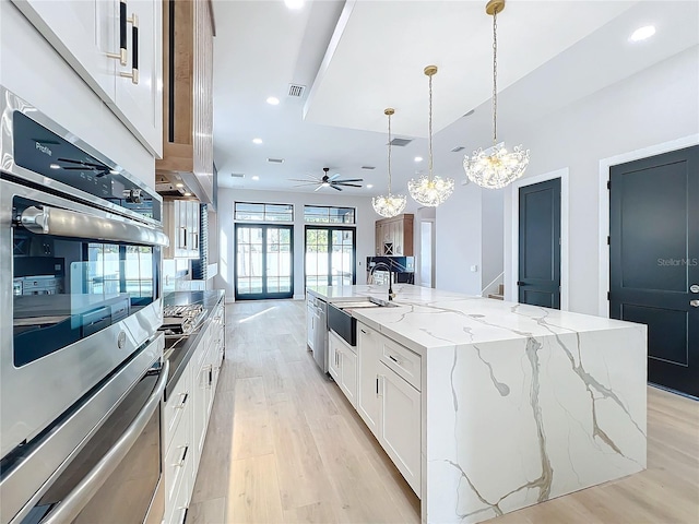 kitchen with ceiling fan with notable chandelier, a large island with sink, white cabinets, and pendant lighting