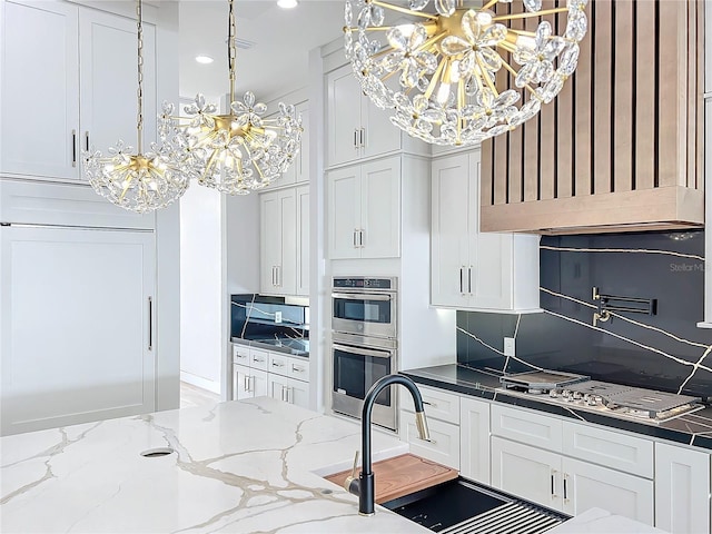 kitchen featuring white cabinetry, appliances with stainless steel finishes, backsplash, a notable chandelier, and sink