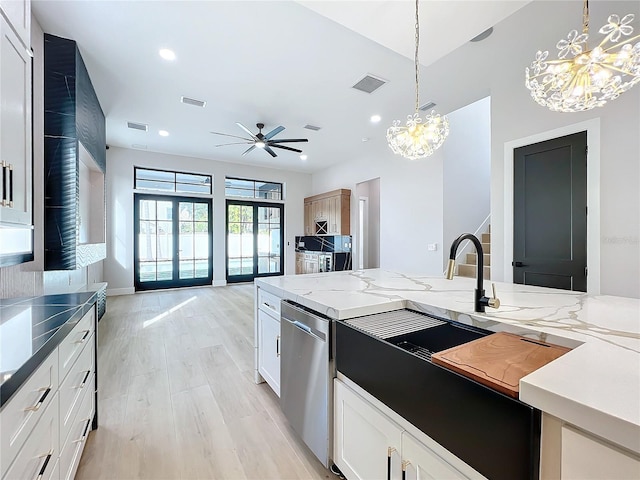 kitchen with stainless steel dishwasher, white cabinetry, hanging light fixtures, dark stone counters, and ceiling fan with notable chandelier