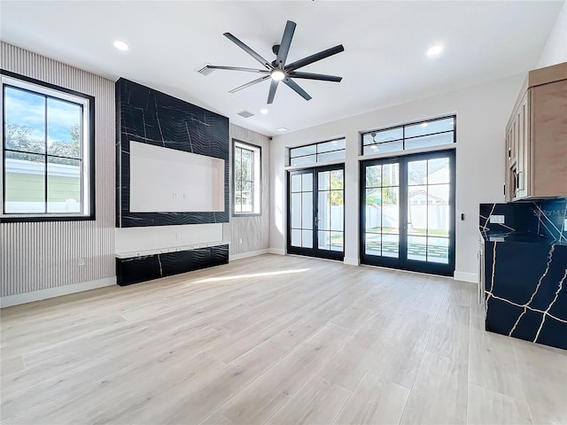 unfurnished living room featuring ceiling fan, french doors, a wealth of natural light, and light hardwood / wood-style floors