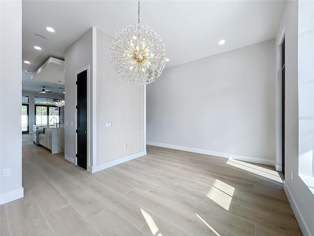 unfurnished dining area with sink, ceiling fan with notable chandelier, and light hardwood / wood-style floors