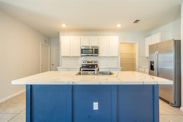 kitchen with a kitchen island with sink, white cabinets, light tile patterned floors, light stone counters, and stainless steel appliances