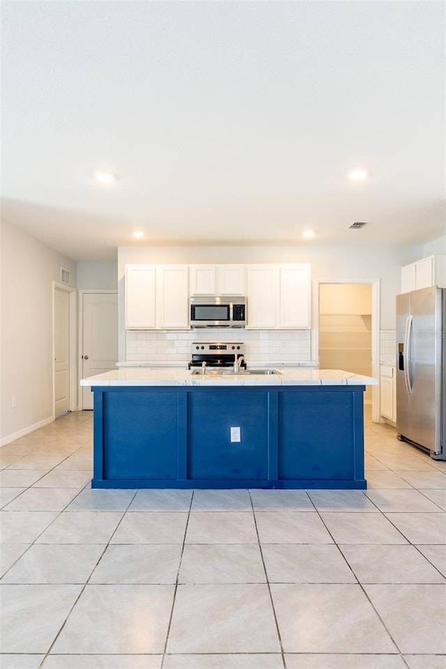 kitchen with decorative backsplash, stainless steel appliances, light tile patterned floors, a center island with sink, and white cabinetry