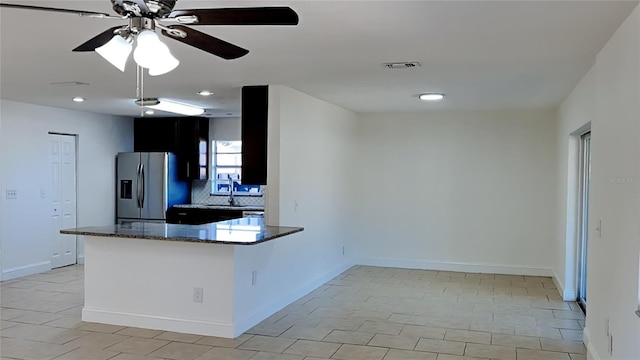 kitchen with sink, tasteful backsplash, stainless steel fridge with ice dispenser, kitchen peninsula, and dark stone countertops