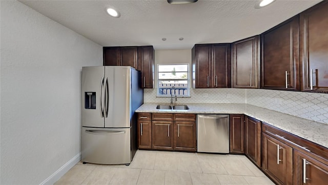 kitchen with decorative backsplash, light stone countertops, dark brown cabinets, stainless steel appliances, and sink