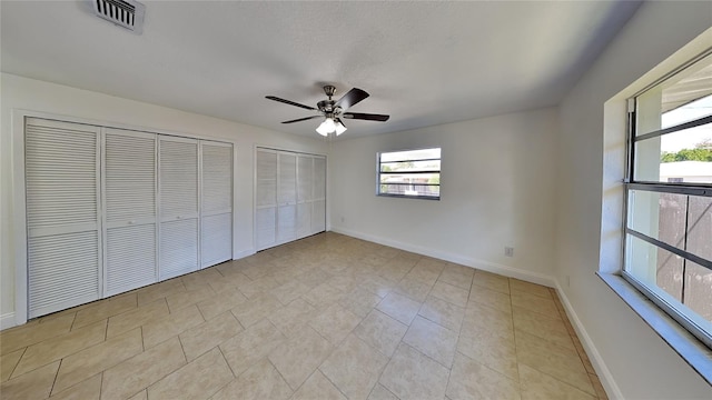 unfurnished bedroom with multiple closets, ceiling fan, and light tile patterned floors