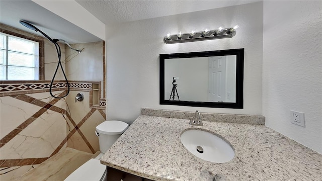 bathroom with vanity, a tile shower, a textured ceiling, and toilet