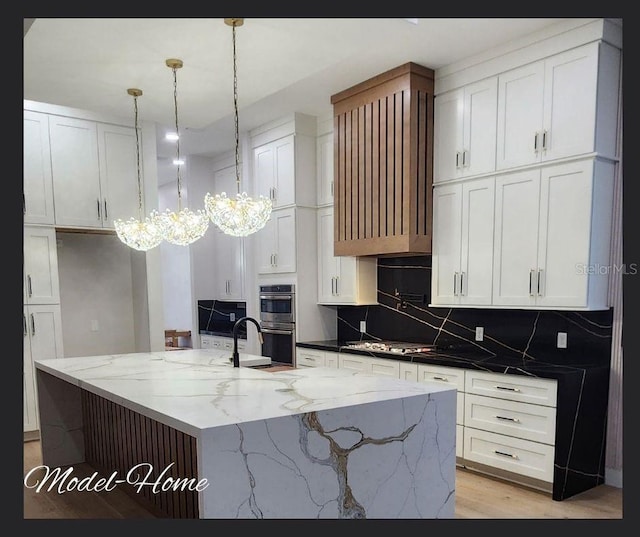 kitchen with a center island with sink, hanging light fixtures, double oven, a notable chandelier, and white cabinetry