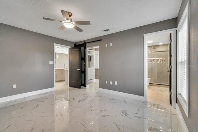 unfurnished bedroom featuring ensuite bathroom, a textured ceiling, ceiling fan, a barn door, and a spacious closet