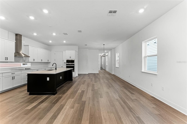 kitchen with sink, light hardwood / wood-style floors, wall chimney exhaust hood, and an island with sink