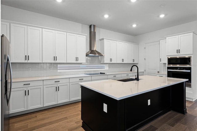 kitchen with wall chimney exhaust hood, dark wood-type flooring, black appliances, sink, and a center island with sink