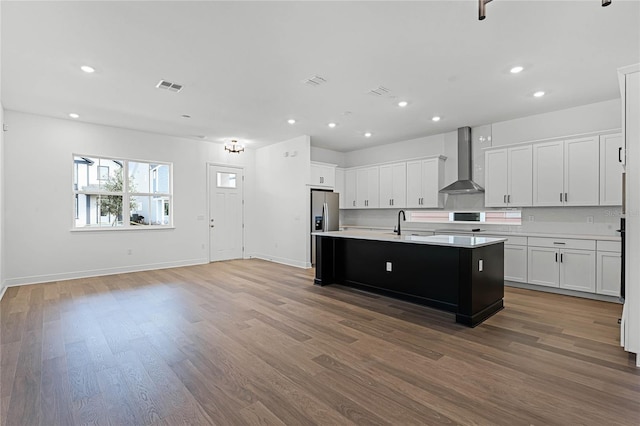 kitchen featuring stainless steel refrigerator with ice dispenser, wall chimney exhaust hood, an island with sink, dark hardwood / wood-style flooring, and white cabinetry