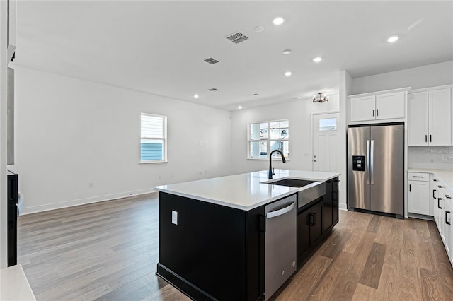 kitchen featuring a kitchen island with sink, light hardwood / wood-style flooring, white cabinets, and appliances with stainless steel finishes