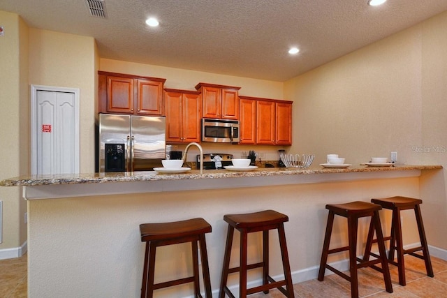 kitchen with light stone counters, kitchen peninsula, a textured ceiling, a kitchen bar, and appliances with stainless steel finishes