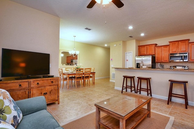 living room featuring ceiling fan with notable chandelier, light tile patterned flooring, and a textured ceiling