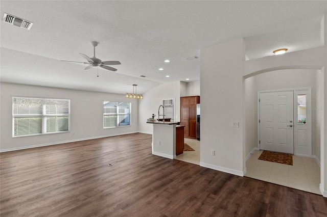 unfurnished living room with lofted ceiling, sink, a textured ceiling, dark hardwood / wood-style flooring, and ceiling fan with notable chandelier