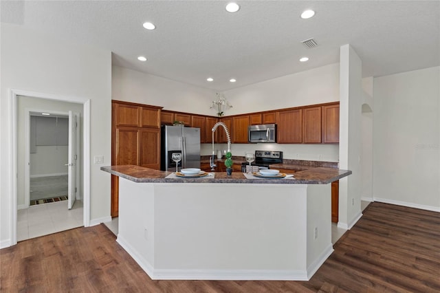 kitchen with stainless steel appliances, dark hardwood / wood-style floors, a center island with sink, and a textured ceiling