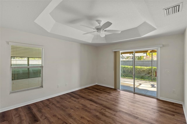 spare room with ceiling fan, a tray ceiling, dark hardwood / wood-style flooring, and a wealth of natural light