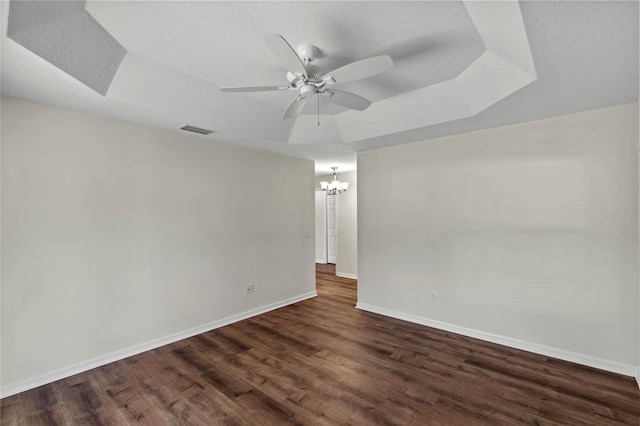 empty room featuring dark hardwood / wood-style floors, ceiling fan with notable chandelier, a textured ceiling, and a tray ceiling