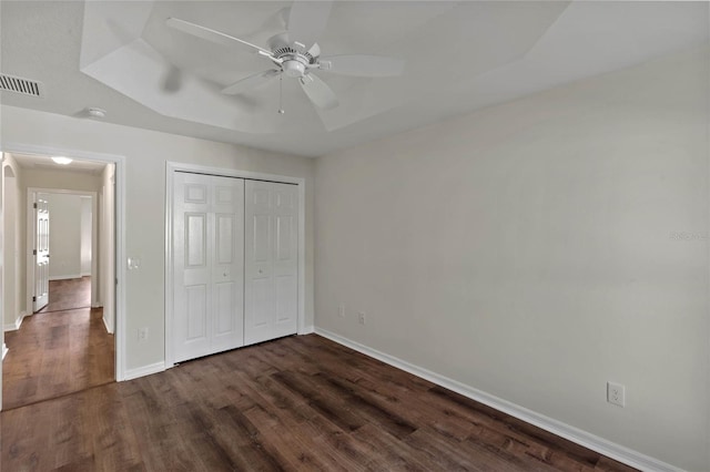 unfurnished bedroom with a closet, dark wood-type flooring, ceiling fan, and a tray ceiling