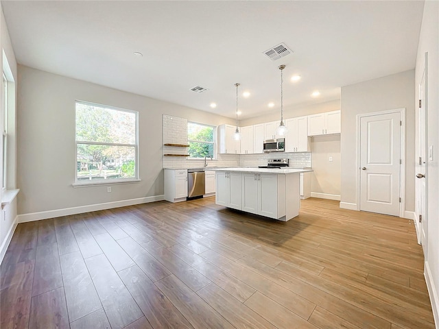 kitchen featuring pendant lighting, a center island, stainless steel appliances, and white cabinetry