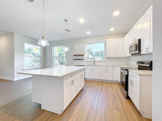 kitchen featuring appliances with stainless steel finishes, light hardwood / wood-style flooring, a center island, white cabinetry, and hanging light fixtures