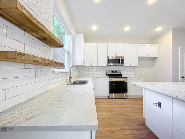 kitchen with tasteful backsplash, stainless steel appliances, sink, light hardwood / wood-style floors, and white cabinetry