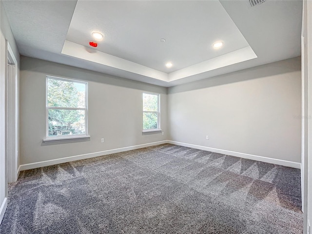 empty room featuring dark colored carpet and a tray ceiling