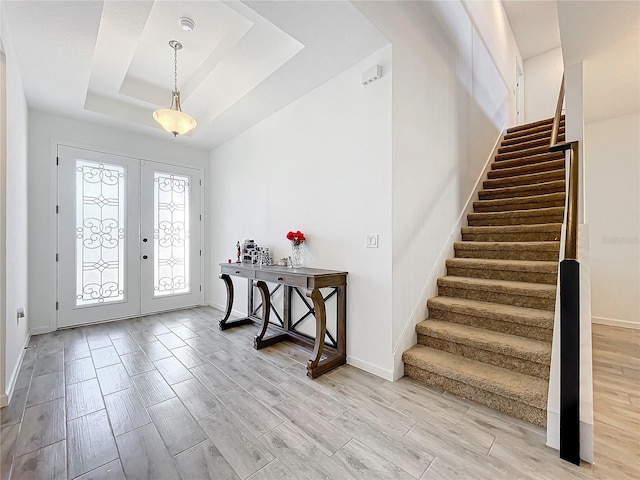 entrance foyer with light wood-type flooring, a tray ceiling, and french doors