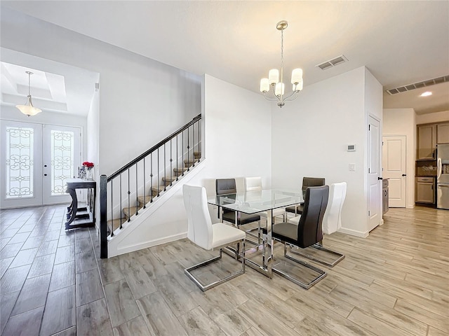 dining space featuring light wood-type flooring, french doors, a tray ceiling, and a chandelier