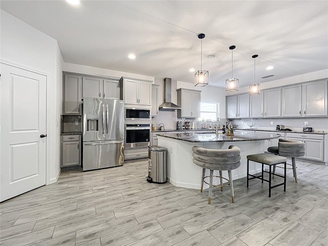 kitchen with wall chimney range hood, a breakfast bar area, decorative light fixtures, a kitchen island, and stainless steel appliances