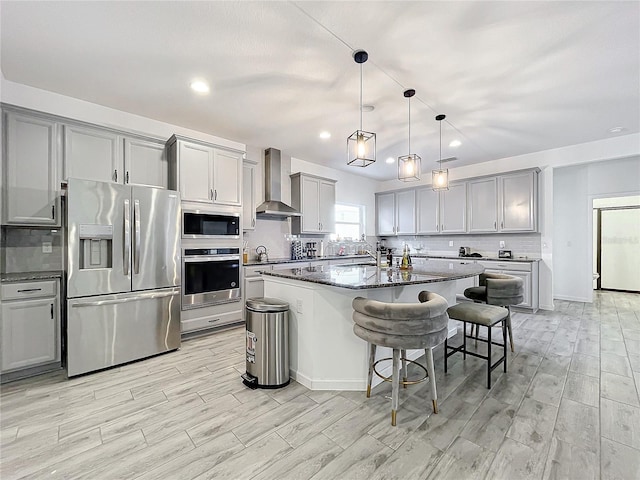 kitchen with a breakfast bar area, a center island with sink, wall chimney exhaust hood, and stainless steel appliances