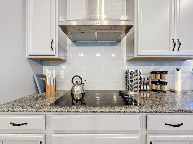 kitchen with black electric stovetop, wall chimney exhaust hood, tasteful backsplash, stone countertops, and white cabinetry