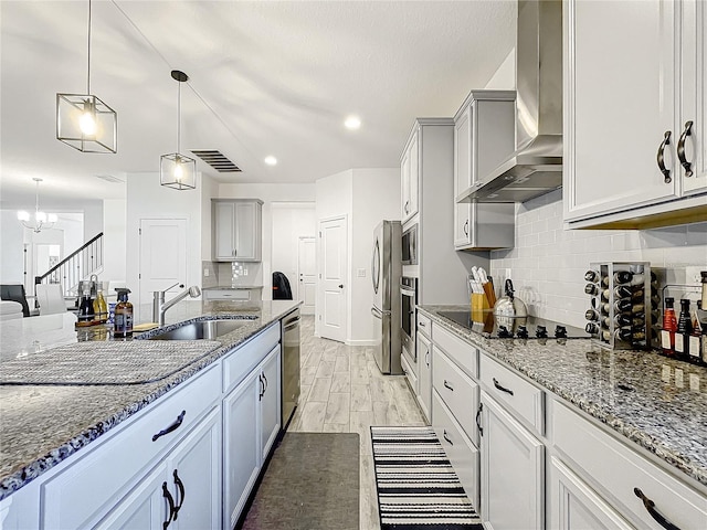 kitchen with appliances with stainless steel finishes, wall chimney exhaust hood, sink, decorative light fixtures, and a chandelier