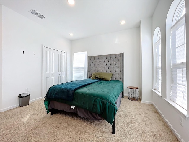 bedroom with a closet, light carpet, and multiple windows