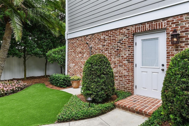 view of exterior entry featuring fence, a lawn, and brick siding