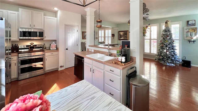 kitchen featuring sink, dark wood-type flooring, hanging light fixtures, stainless steel appliances, and white cabinets