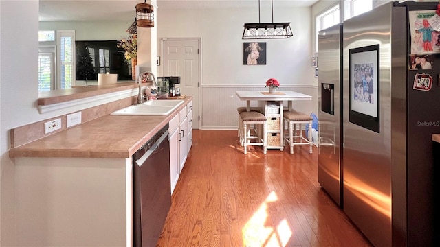 kitchen with light wood-type flooring, stainless steel appliances, sink, white cabinetry, and hanging light fixtures