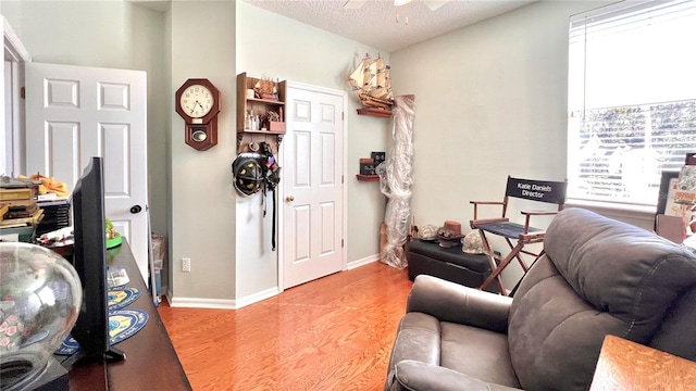 living room featuring ceiling fan, light hardwood / wood-style floors, and a textured ceiling