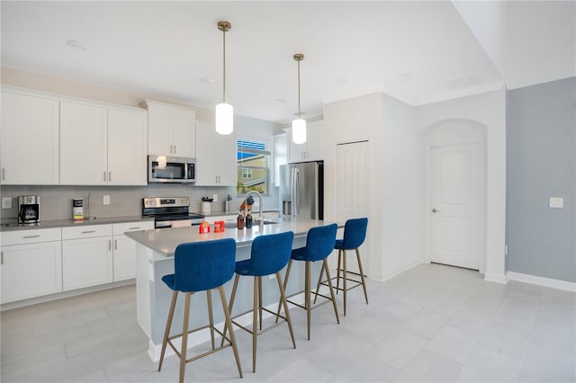 kitchen featuring a center island with sink, white cabinets, pendant lighting, stainless steel appliances, and backsplash