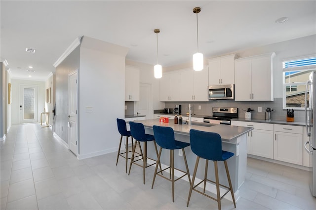 kitchen featuring white cabinetry, appliances with stainless steel finishes, a center island with sink, and decorative light fixtures