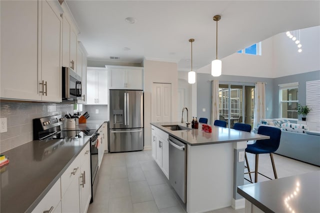 kitchen with appliances with stainless steel finishes, decorative light fixtures, white cabinetry, sink, and a center island with sink