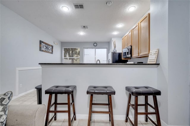 kitchen featuring a kitchen breakfast bar, kitchen peninsula, a textured ceiling, and appliances with stainless steel finishes