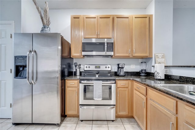 kitchen featuring appliances with stainless steel finishes, light brown cabinets, dark stone counters, and light tile patterned flooring