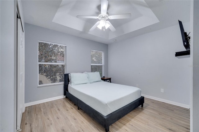 bedroom featuring light hardwood / wood-style floors, a raised ceiling, and ceiling fan